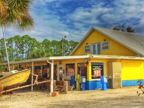 A colorful yellow building with a boat in front, surrounded by palm trees and a blue sky with scattered clouds.