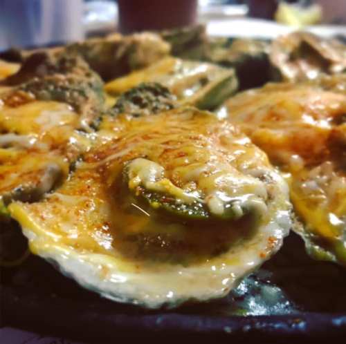 Grilled oysters topped with cheese and spices, served on a sizzling platter.