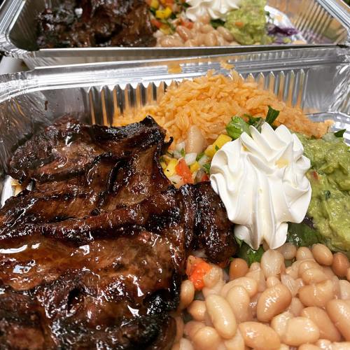 A close-up of a meal featuring grilled meat, rice, beans, guacamole, and sour cream in a takeout container.