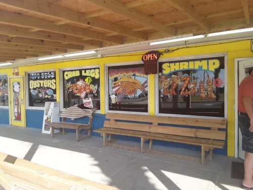 Colorful restaurant exterior featuring signs for oysters, crab legs, and shrimp, with a bench and "Open" sign.