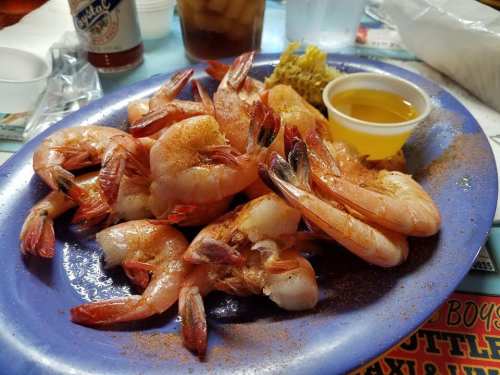 A blue plate filled with seasoned shrimp, a small cup of dipping sauce, and a side of pickles.