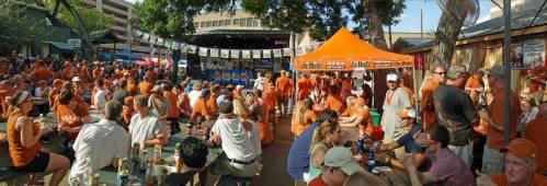 A lively outdoor gathering with a crowd wearing orange, enjoying food and drinks at a festive event.