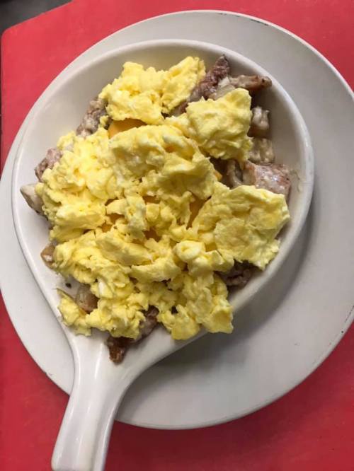 A dish featuring fluffy scrambled eggs on top of cooked meat, served in a white oval dish on a red surface.