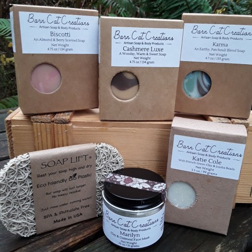 A collection of handmade soaps and a facial mask from Barn Cat Creations, displayed on a wooden surface.