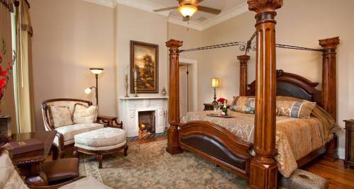 Elegant bedroom featuring a four-poster bed, cozy seating area, and a decorative fireplace. Warm, inviting decor.