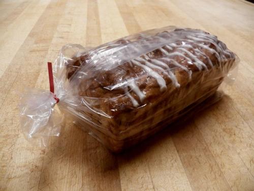 A loaf of bread in a clear plastic bag, tied with a red twist tie, resting on a wooden surface.