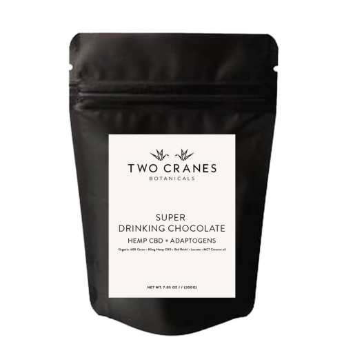 A black pouch labeled "Two Cranes Botanicals Super Drinking Chocolate" with hemp CBD and adaptogens.
