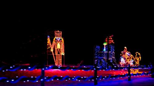 Colorful holiday lights display featuring a nutcracker, a sleigh, and festive decorations against a dark background.