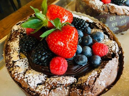 A rich chocolate cake topped with fresh strawberries, blackberries, blueberries, and raspberries, dusted with powdered sugar.