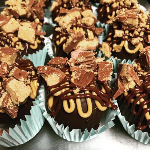Delicious chocolate treats topped with peanut butter drizzle and crushed candy, arranged in blue cupcake liners.