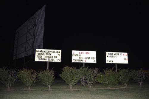 A nighttime view of a drive-in movie theater sign displaying movie titles and showtimes.