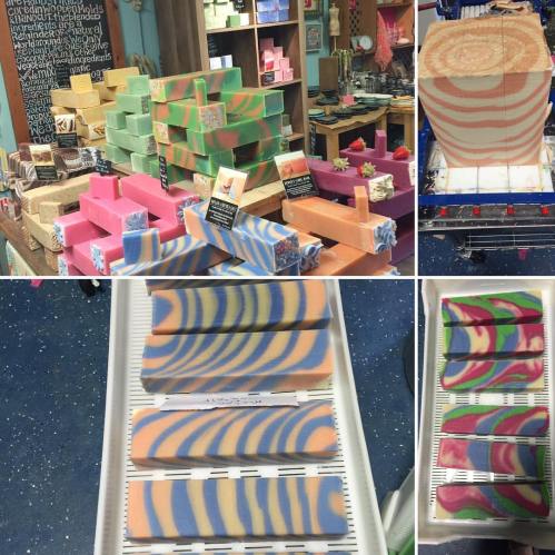 A display of colorful handmade soaps in various shapes and patterns, arranged on shelves and trays.
