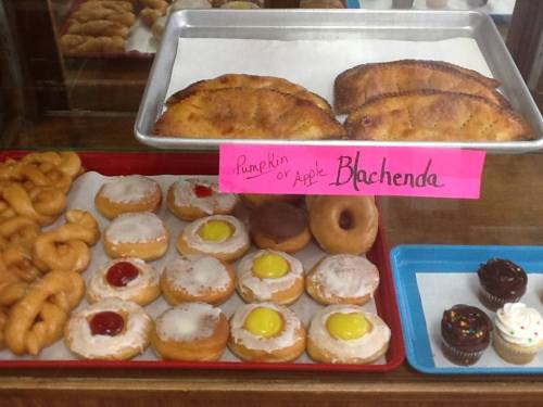 A display of assorted pastries, including donuts, filled pastries, and cupcakes, with a sign for pumpkin or apple options.
