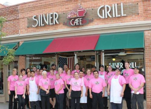 A large group of smiling staff in pink shirts stands outside Silver Grill Café, with an American flag in the background.