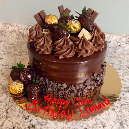 A chocolate birthday cake decorated with chocolate swirls, candies, and strawberries, with "Happy 16th Birthday Leonard" written on it.