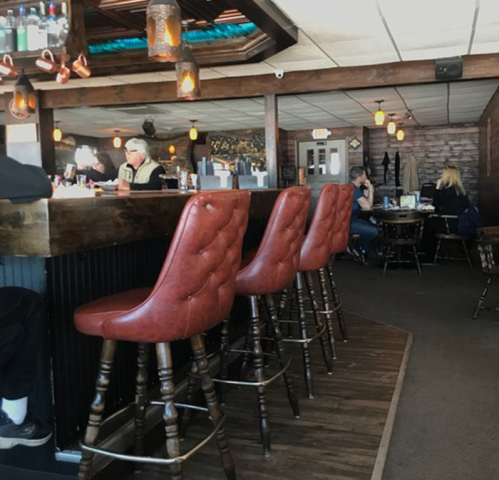 A cozy restaurant interior featuring wooden bar stools, a bar area, and patrons enjoying their meals.