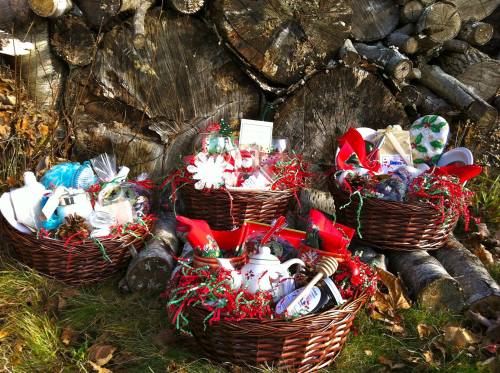 Four festive gift baskets filled with holiday treats and decorations, set against a backdrop of stacked logs.