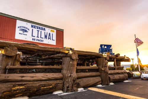 A rustic building with a large sign reading "Nevada LILWAL" and a blue tractor on the roof, set against a sunset sky.