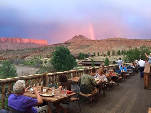 A scenic outdoor dining area with people enjoying meals, surrounded by mountains and a colorful sunset.