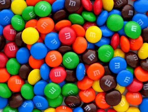 A colorful assortment of M&M candies in various shades, including blue, green, yellow, red, orange, and brown.