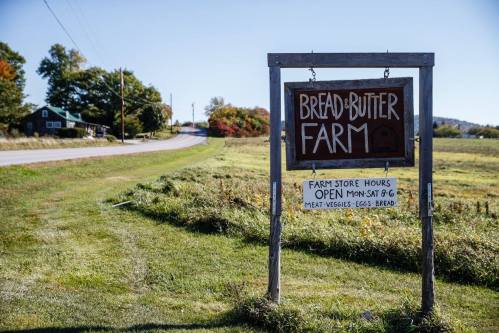 Sign for Bread and Butter Farm with store hours, set in a rural landscape with a road and fields.