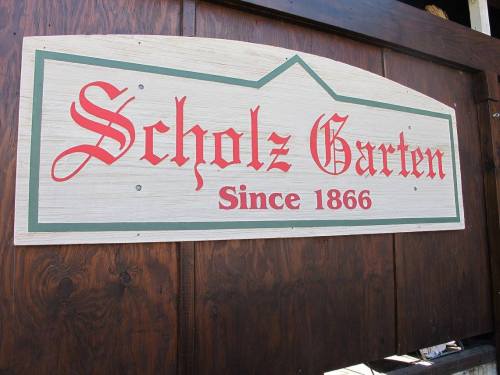 Sign for "Scholz Garten" with a decorative font, stating "Since 1866," mounted on a wooden background.