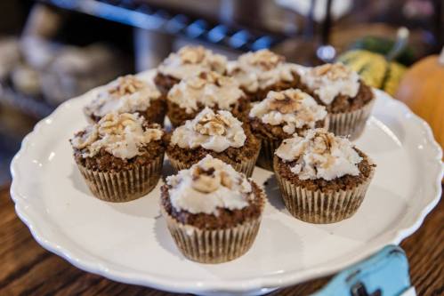 A plate of freshly baked cupcakes topped with creamy frosting and walnuts, displayed on a wooden table.