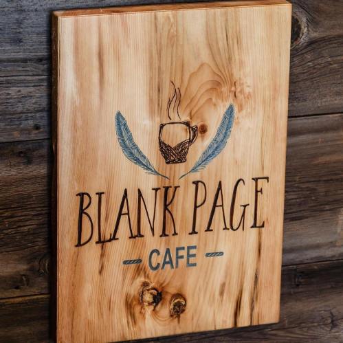 Wooden sign for "Blank Page Cafe" featuring a coffee cup and decorative feathers.