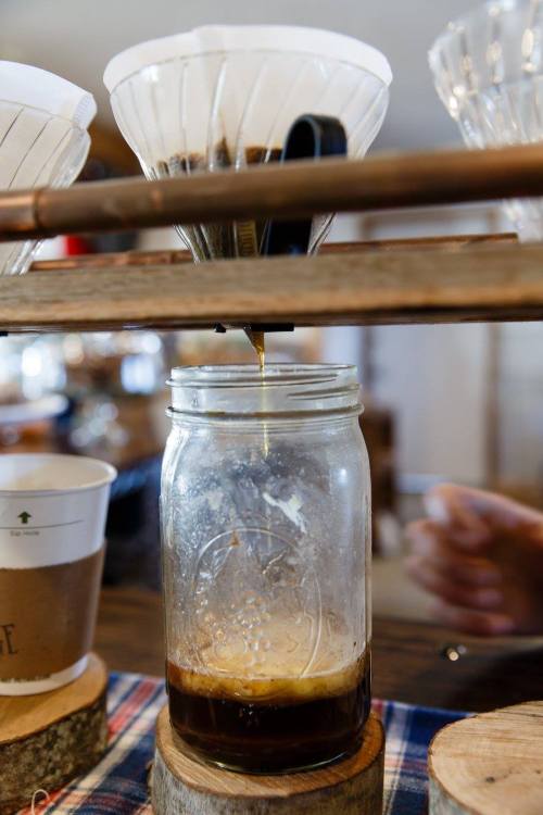 A coffee brewing setup with a glass jar collecting freshly brewed coffee from a filter above.