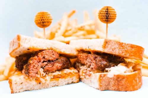 A close-up of a sandwich with a meat patty and sauerkraut, served with golden fries in the background.