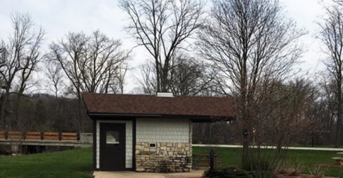 A small, rustic building with a stone and wood exterior, surrounded by trees and grass in a park setting.