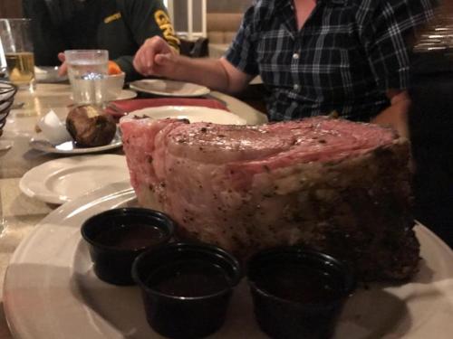 A large, juicy prime rib served on a plate with two small cups of sauce, set on a dining table.