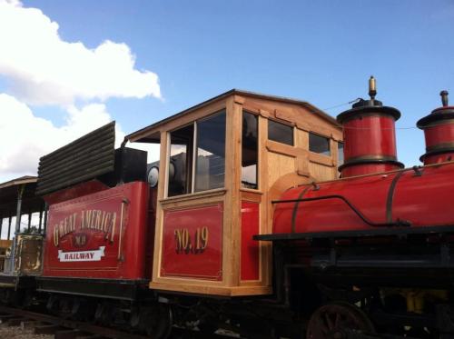 A vintage steam locomotive with a red and wooden cabin, labeled "Great America Railway No. 19," parked under a blue sky.