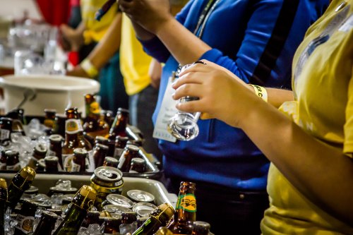 People serving drinks from a table filled with ice and various bottles and cans of beverages.