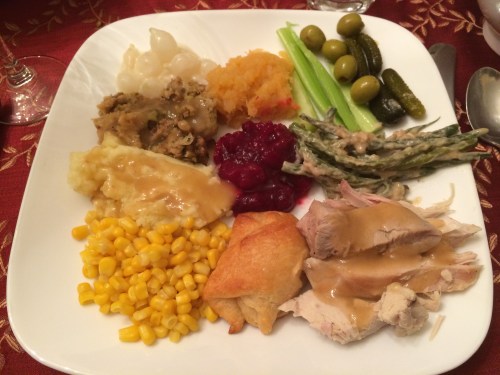 A plate of Thanksgiving food featuring turkey, stuffing, mashed potatoes, corn, green beans, cranberry sauce, and more.