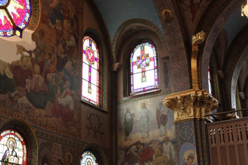 Interior of a church featuring colorful stained glass windows and detailed murals on the walls.
