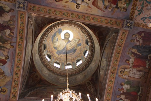 Ceiling of a church featuring a central dome with a depiction of Christ and colorful frescoes of saints around the edges.