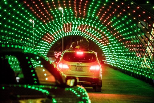 A car drives through a colorful light tunnel decorated with red and green lights during a festive event.