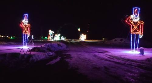 Colorful holiday lights illuminate a snowy path, featuring large toy soldier figures and festive decorations.