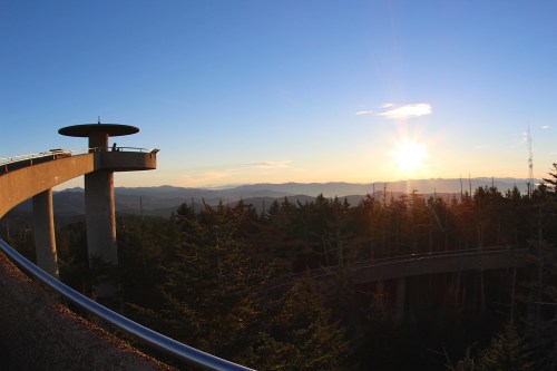 A scenic overlook with a circular platform at sunset, surrounded by mountains and trees.