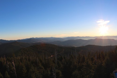 A panoramic view of mountains at sunset, with a clear sky and sun casting light over the landscape.