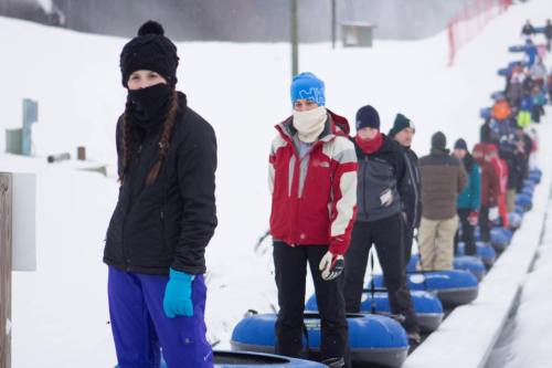 A group of people in winter clothing waiting in line for snow tubing on a snowy day.