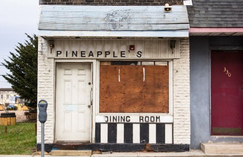 Abandoned restaurant facade with boarded windows, featuring a sign that reads "Pineapple's Dining Room."