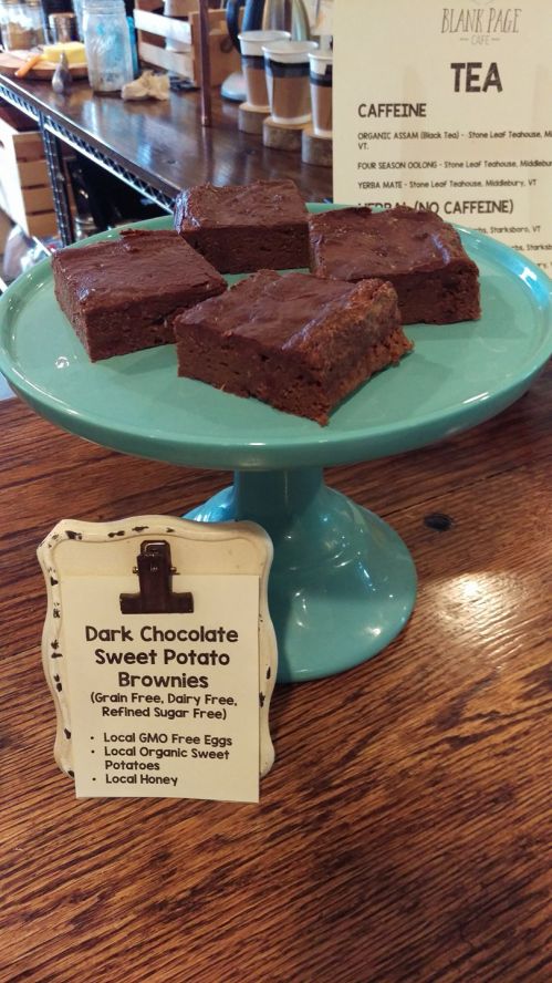 A plate of dark chocolate sweet potato brownies on a teal stand, with a sign listing their ingredients and benefits.