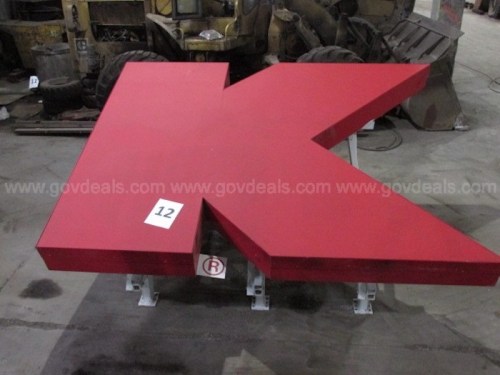 Large red letter "K" sign on a concrete floor, with a white number "12" sticker attached.