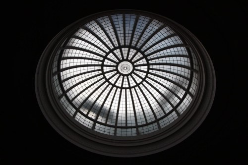 A circular stained glass dome with a geometric pattern, illuminated by natural light against a dark background.
