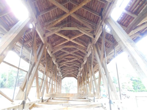Interior view of a wooden covered bridge, showcasing exposed beams and a rustic ceiling. Natural light filters through.
