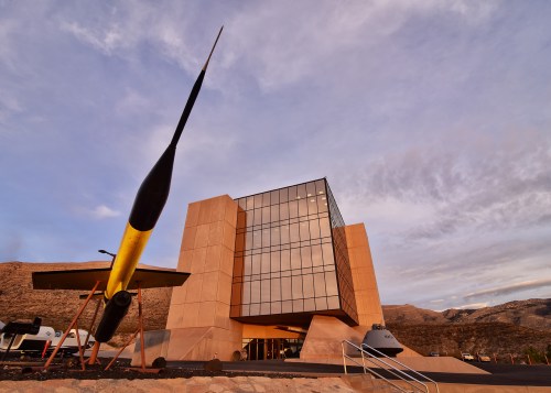 Modern building with large glass facade, featuring a yellow propeller sculpture in the foreground against a mountainous backdrop.