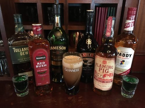 A selection of Irish whiskeys and a pint of Guinness on a bar, with shot glasses in the foreground.