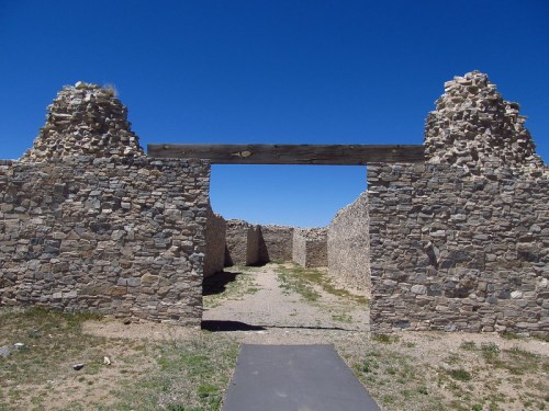 Stone ruins with a clear blue sky above, featuring an archway and a pathway leading through the structure.